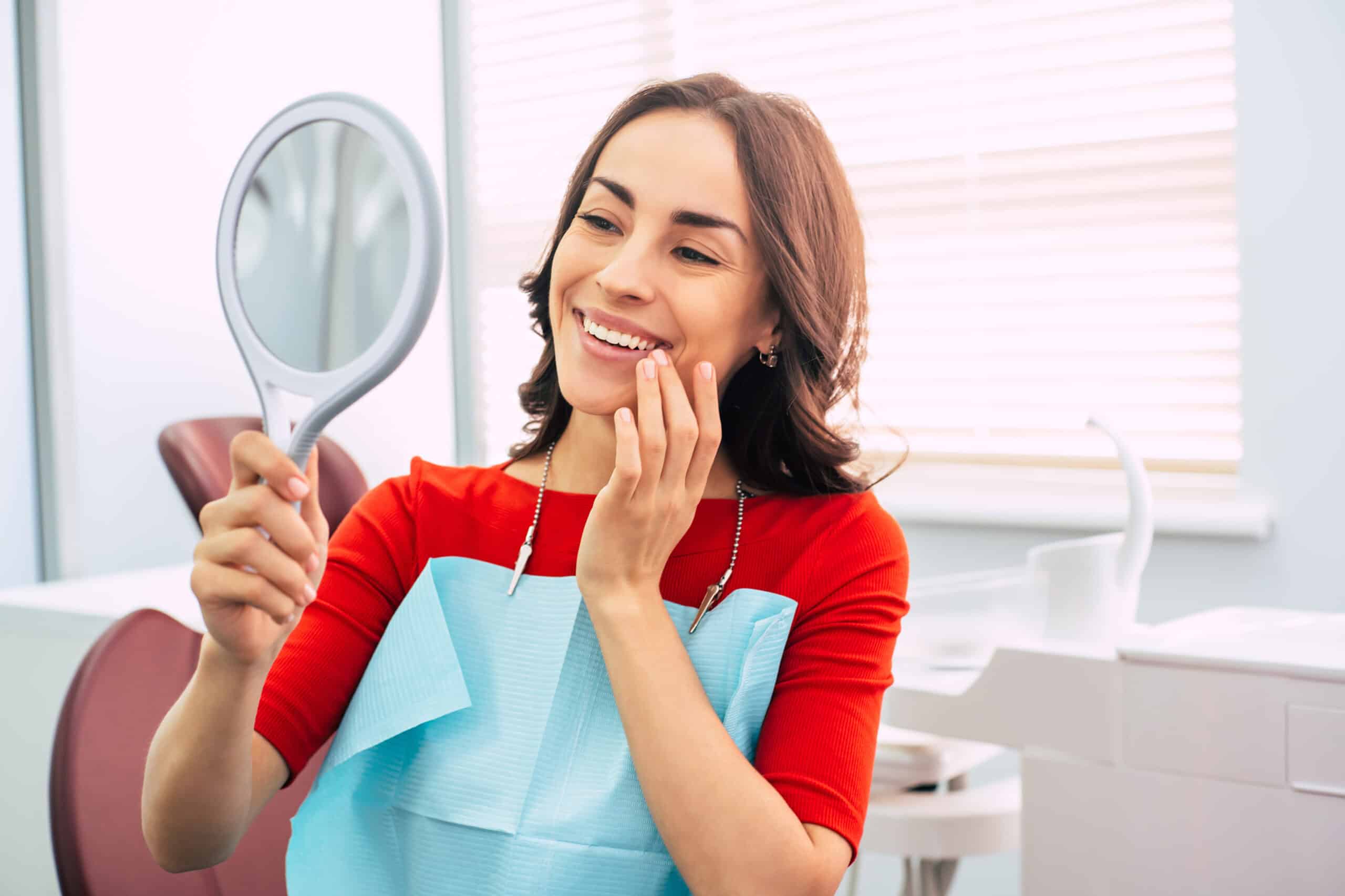 A young female smiling watching her shining teeth in mirror after cosmetic dentistry