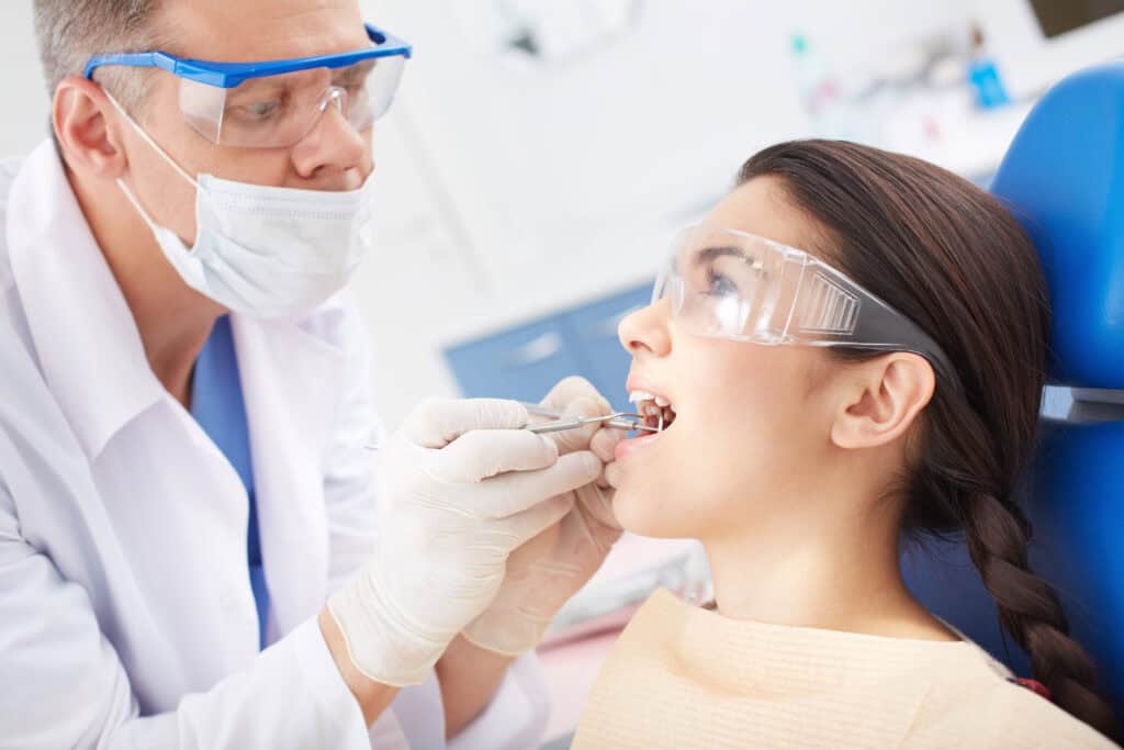 A young girl is sitting in a dental clinic and getting its restorative procedures done by the young male dentist.