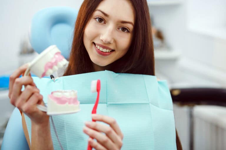 Girl with toothbrush in hand and teeth North Shore Cosmetic and Implant Dentistry Happy patient holding a toothbrush and dental mold in a dental office, promoting comfortable dental visits and oral health education.