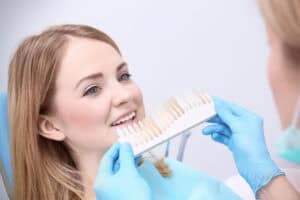 Dentist checking and selecting color of young womans teeth North Shore Cosmetic and Implant Dentistry Ultra Thin Veneers No Prep Veneers Dentist selecting teeth shade for a young womans smile makeover