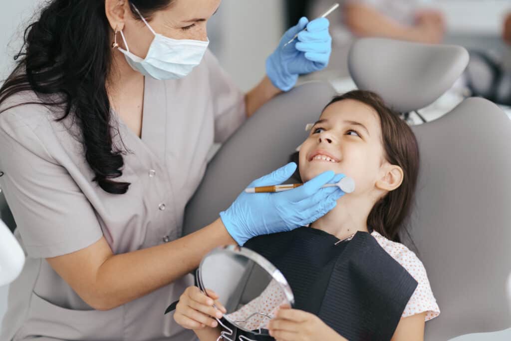 Pediatric dentist providing gentle dental care to a smiling child during a dental exam in Great Neck, NY.