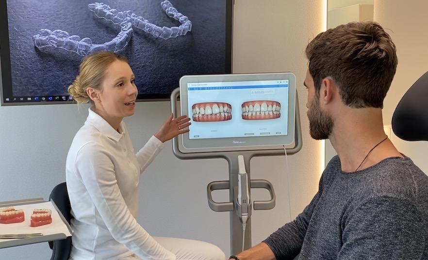 Dentist explaining Invisalign treatment progression to a patient using digital images of teeth alignment.