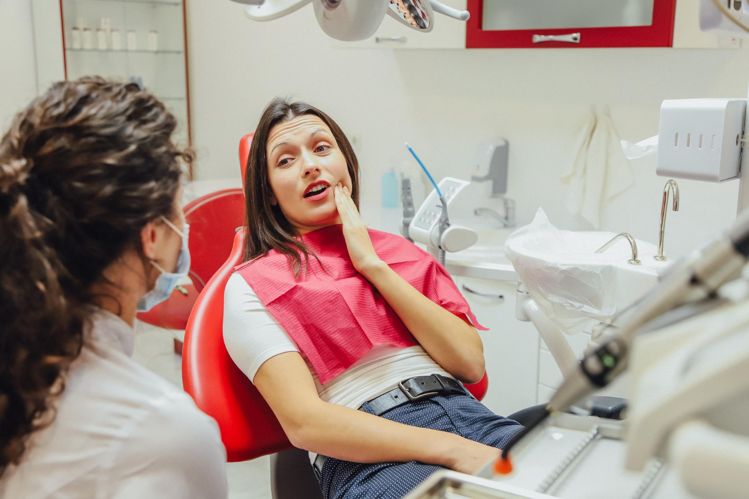 Patient experiencing tooth pain during a dental visit while discussing root canal symptoms and dental treatment with a dentist.