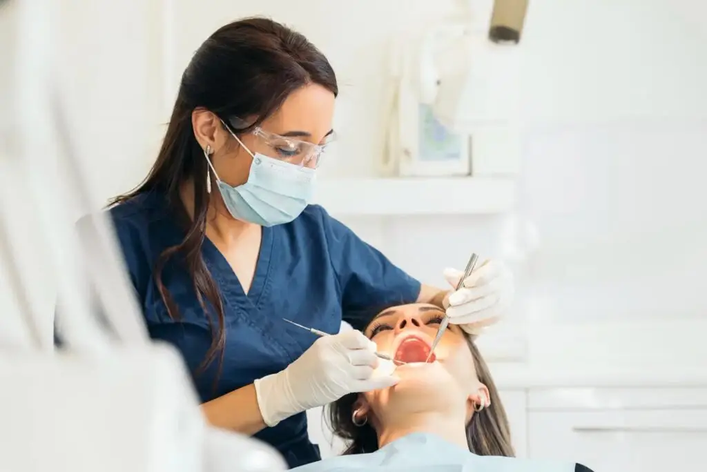 Dentist in mask and gloves examining a patient's open mouth with dental tools